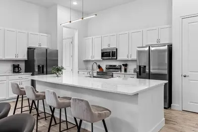 a white kitchen with a large island with bar stools at Brand NEW 11 Bedrooms At Sonoma in Kissimmee