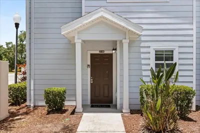 a white house with a brown door and bushes at 4 Bedrooms 3 Bathrooms Lucaya Village 23-108 in Kissimmee
