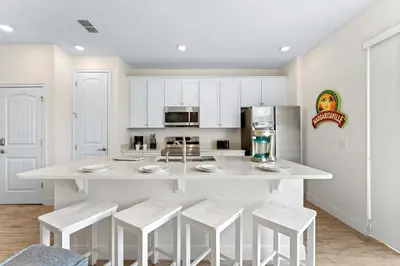 a kitchen with a large white island with stools at Capri Sunset in Orlando