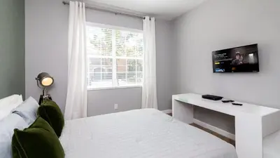a white bedroom with a bed and a tv on the wall at Casa de Kissimmee Sleeps up to 13 Guests in Kissimmee