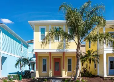 a yellow house with a red door and palm trees at Parrotfish Place - Stay for 6 in Orlando