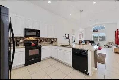 a large kitchen with white cabinets and black appliances at Luxury Family Villa With Pool & Bbq Near Disney! in Kissimmee