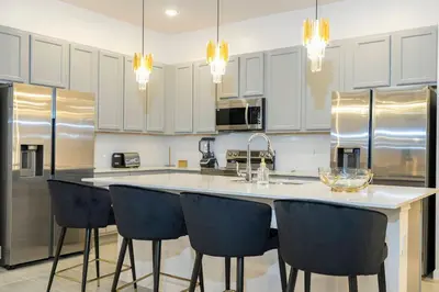 a kitchen with white cabinets and a island with bar chairs at Brand New 12 Bedrooms Single Family Paradiso 85HI in Orlando