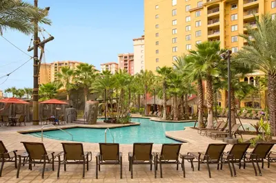 a pool with chairs and palm trees and buildings at Wyndham Bonnet Creek 2BR Apartment with Resort Access in Orlando