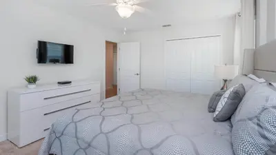 a white bedroom with a bed and a tv at Storey Lake Villa in Kissimmee