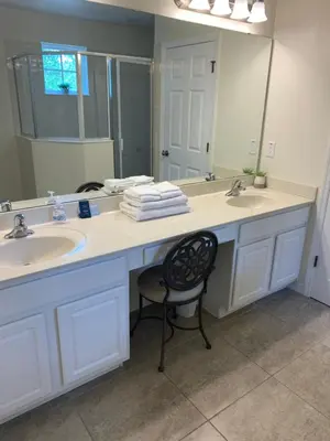 a bathroom with two sinks and a mirror and a chair at Resort 4 Br 3 Ba Private Pool Home & Lake View near Disney & Universal in Kissimmee