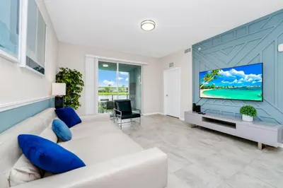 a living room with a white couch and a large screen tv at 2BR Family Condo Near Disney, Universal and More in Kissimmee