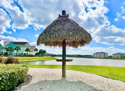 a straw umbrella sitting on a sidewalk near a body of water at Waves of Relaxation - For 8 in Orlando