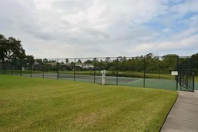 a tennis court with a fence and a grass field at 4-Bed Home Near Disney Private Pool in Kissimmee