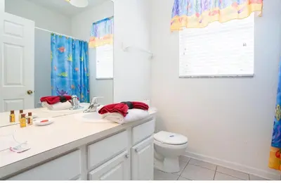 a bathroom with a toilet and a sink and a mirror at DREAM Vacation BY A3G in Orlando