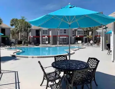 a table and chairs with an umbrella next to a pool at Condo Near Disney No Resort Fee Free Parking in Orlando