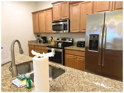 a kitchen with wooden cabinets and a stainless steel refrigerator at Disney Getaway Townhouse with Private Pool. Book Now SLR484 in Kissimmee