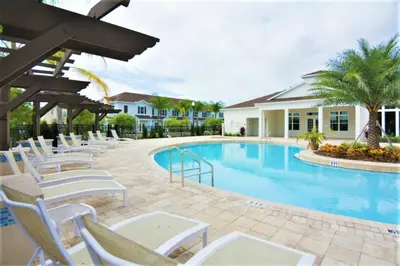 a swimming pool with white chairs next to a house at Disney Getaway Townhouse with Private Pool. Book Now WLV82 in Kissimmee