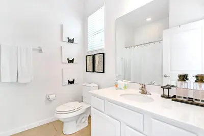 a white bathroom with a toilet and a sink at UPSTAY- 10BR Mansion wPrivate Pool and Games Room in Kissimmee