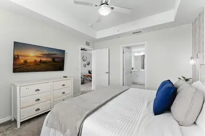 a white bedroom with a bed and a tv on the wall at Elegant 2BR in Storey Lake Top Location in Kissimmee