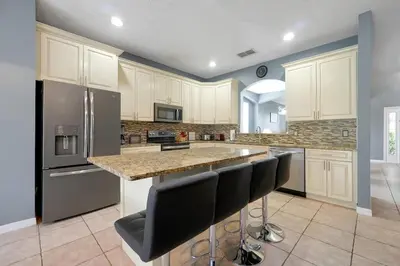 a kitchen with white cabinets and a island with bar stools at Ever After Estate in Kissimmee