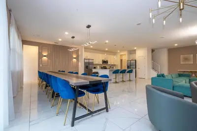 a kitchen and living room with a long table and blue chairs at Stunning Mansion 15 ensuites in Kissimmee