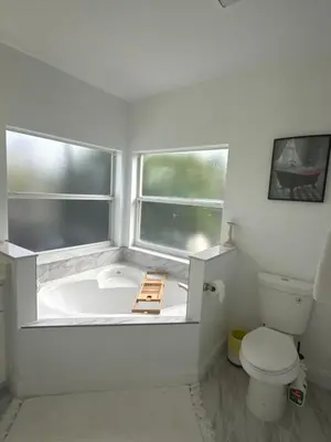 a bathroom with a tub and a toilet and two windows at Cozy family house near Disney,epic and universal in Orlando