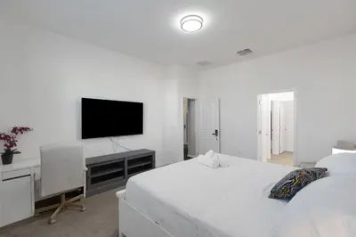 a white bedroom with a bed and a television at Cozy Rooms In An Elegant House in Kissimmee