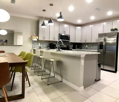 a kitchen with white cabinets and a kitchen island with green chairs at NEW Home 3 Bedrooms Water View Disney Universal in Kissimmee