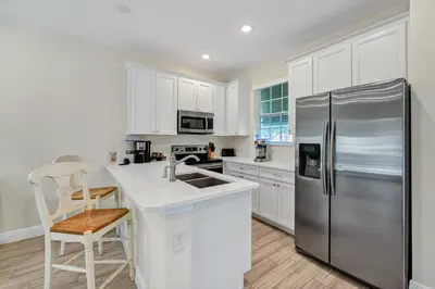 a kitchen with white cabinets and a stainless steel refrigerator at Lush Garden Oasis Cottage Near Disney With Margaritaville Resort And Island H2O Waterpark Access - 8016Ff in Orlando