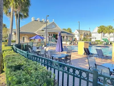 a pool with chairs and tables and a umbrella at 3 Bedroom 2 Bathroom Villas At Seven Dwarfs 25-105 in Kissimmee
