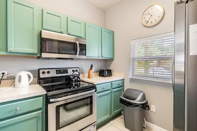 a kitchen with green cabinets and a stove and a clock at Family Townhome Near Disney w Heated Pool in Kissimmee