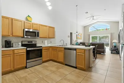 a kitchen with wooden cabinets and appliances and a living room at Cozy No-Carpet Home Heated Pool Disney in Kissimmee