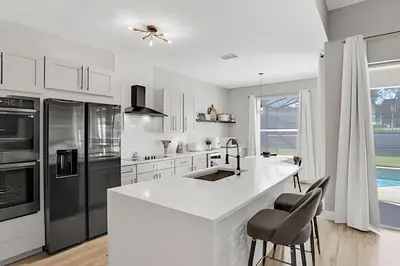 a white kitchen with a large white counter and stools at Luxo 5Q Windsor Hills c/ Piscina e Game Room in Orlando