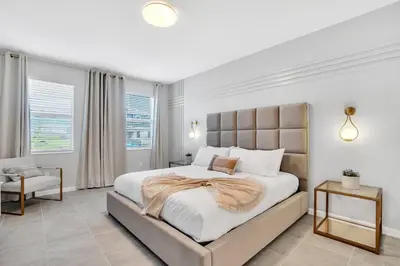 a white bedroom with a large bed and a chair at Disney-Adjacent 15Bd15Ba Oasis With Private Pool in Kissimmee