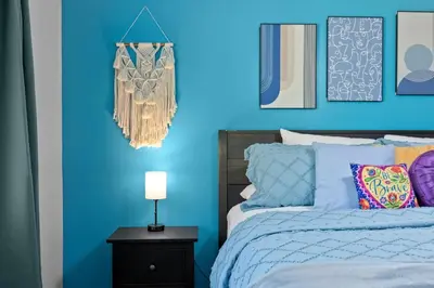 a bedroom with a blue wall with a bed and a lamp at Red Jordan Boho Style Vacation Home in Orlando
