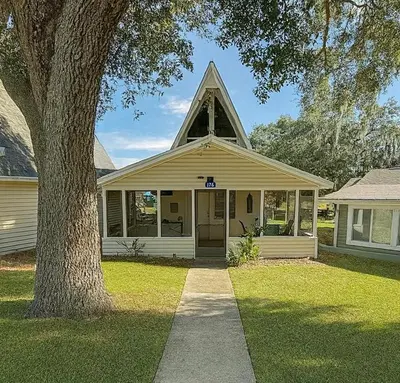 a white house with a pointed roof and a tree at Cottage-pvt Lake & Pool Access Near Disney Wporch in Clermont