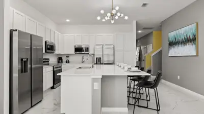a kitchen with white cabinets and a large island with bar chairs at Upstay Veranda Palms Villa Pool Hot Tub & Games in Kissimmee