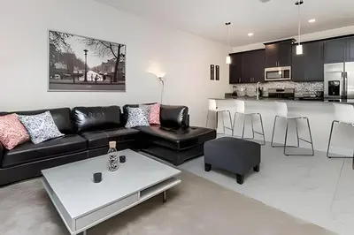 a living room with a black couch and a kitchen at Villa Sanches 4Q c/ Piscina – Storey Lake Resort in Kissimmee