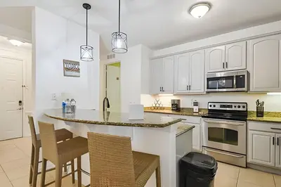 a kitchen with white cabinets and a island with chairs at Apartamento Vista Cay: ao lado do UNIVERSAL in Orlando