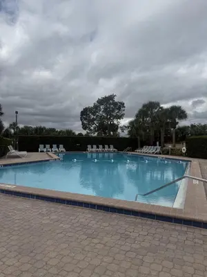 a large swimming pool with lounge chairs and a cloudy sky at Sunny Orlando Oasis - Cozy 2 Bedroom house near Disney in Kissimmee