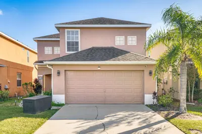 a house with a garage and a palm tree at Modern Resort Getaway 9 Mi to Disney Parks! in Kissimmee