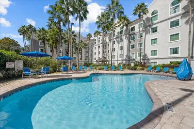 a pool with chairs and umbrellas in front of a building at Suite near Disney, free parking and shuttle to Parks in Orlando