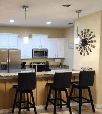 a kitchen with white cabinets and a counter with three chairs at Villa Coco in Kissimmee