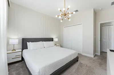 a white bedroom with a bed and a chandelier at 4350 Storey Lake 17 guests near parks poolspa in Kissimmee