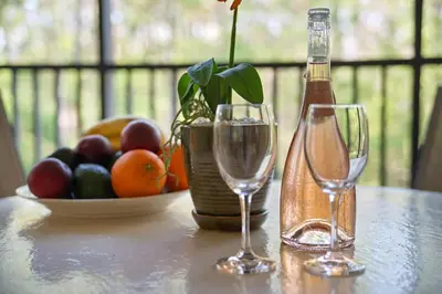 two wine glasses and a bottle on a table with a bowl of fruit at Serene Gem, close to Disney- HEATEDsaltwaterPOOL in Kissimmee