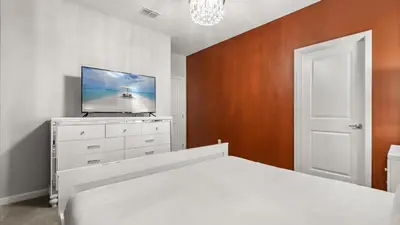 a bedroom with a white bed and a flat screen tv at Upstay Bella Vida Retreat w Pool Cinema and Games in Kissimmee
