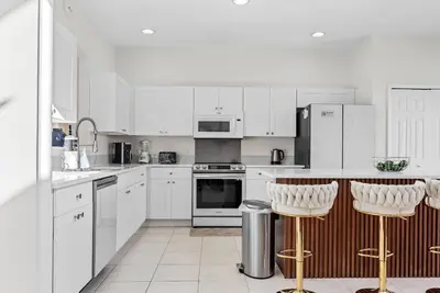 a white kitchen with white cabinets and bar stools at Comfortable 6-Bedroom Getaway Near Top Attractions in Kissimmee