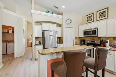 a kitchen with white cabinets and a counter with chairs at Casa aconchegante em Glenbrook perto da Disney in Orlando