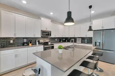 a kitchen with white cabinets and a large island with chairs at Classy 6BR Home with Private Pool in Kissimmee