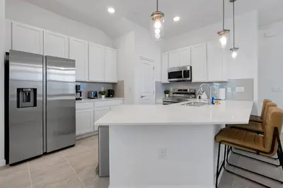 a kitchen with white cabinets and a stainless steel refrigerator at New 5BR Villa Near Disney I Resort Lazy River in Orlando