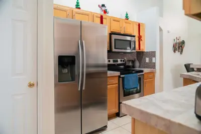 a stainless steel refrigerator in a kitchen with wooden cabinets at Gated Pool Home 20 Min to Disney, Uni, MCO in Kissimmee