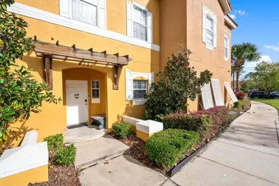 a yellow building with a white door and a sidewalk at Family Escape! HotTub+Grill+Disney! in Kissimmee