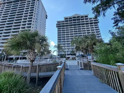 a wooden walkway with two tall buildings and palm trees at Blue Heron Beach Resort Tower 12 FL 1204 Fully Furnished in Orlando