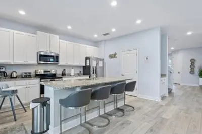 a kitchen with white cabinets and a island with bar stools at 381 Fantastic Home Near Disney 5BD 5BT 14P in Orlando